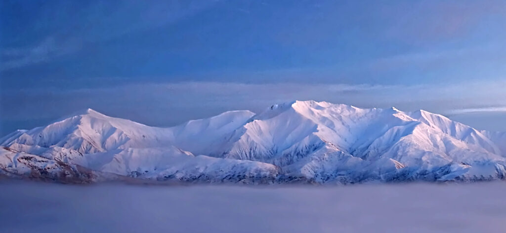 Panoramic sunrise over snow-covered Mt Cardrona above a sea of inversion cloud, Wānaka New Zealand winter driving.