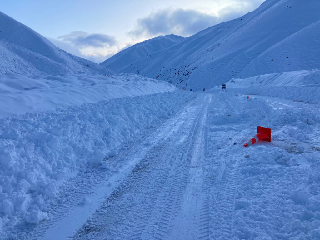 Crown Range road summit after a heavy snow fall. The road reduced to one lane, with a fallen road cone.